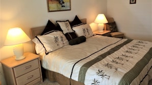 Una cama bien hecha con cubrecama blanco y verde, dos lámparas de noche y una mesita de noche de madera con cajones.
