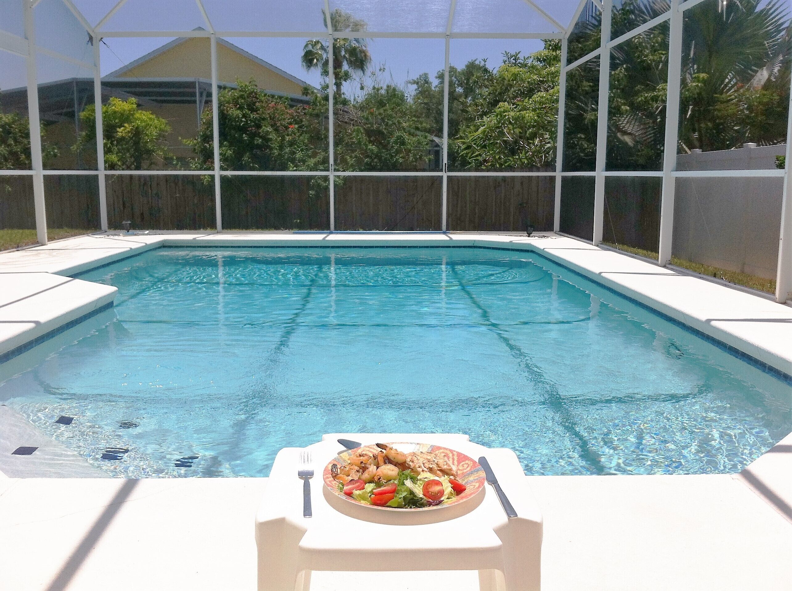A swimming pool with a table and a plate of food in the foreground.