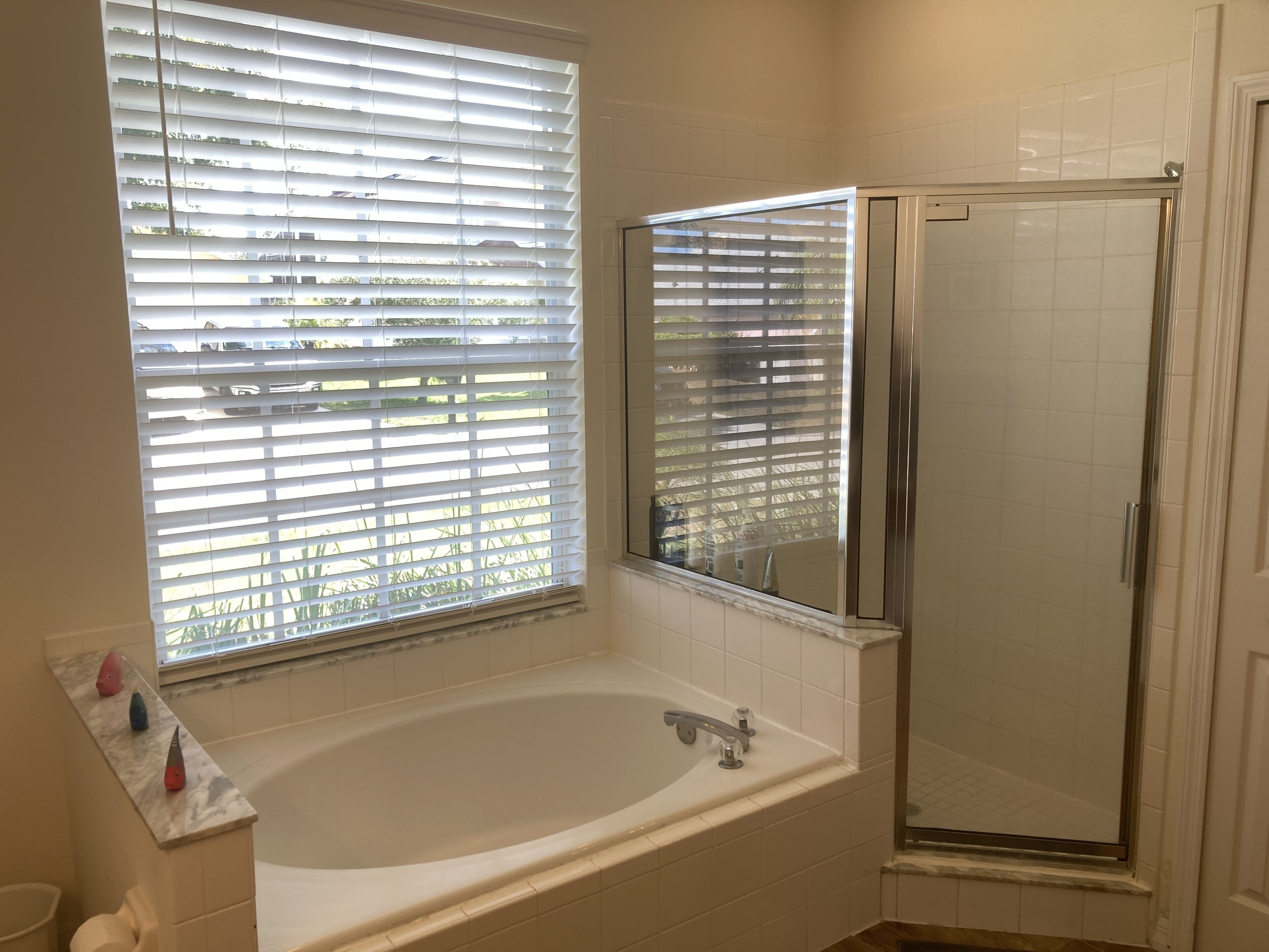 A bathroom with a bathtub, a glass shower enclosure, and a window with blinds.