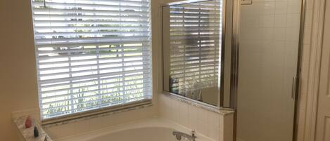 A bathroom with a bathtub, a glass shower enclosure, and a window with blinds.