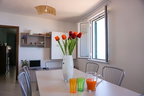A dining area with a white table, chairs, a vase with flowers, and a window with blinds. - Il Terrazzo su Pizzo - panoramic apartment with sea view (Pizzo)
