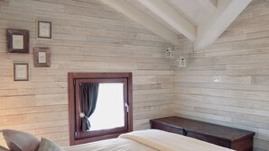 Een slaapkamer met houten wanden, een raam met gordijnen, een bed met kussens en een nachtkastje.