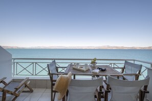 A terrace with a table set for two, overlooking a calm sea and distant mountains.
