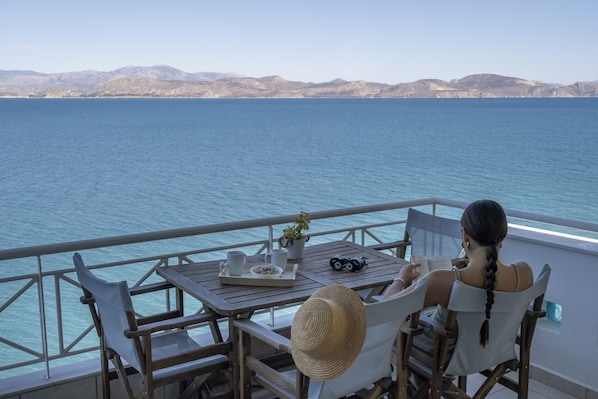 A woman reading at a table with a view of the sea and mountains.