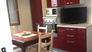 A compact kitchen with a dining table, chairs, a microwave, an oven, and a television.