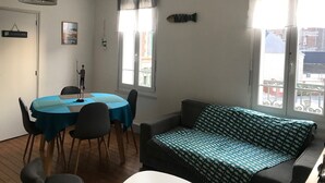Une pièce comprenant une table à manger, des chaises, un canapé, un luminaire suspendu et une fenêtre avec des rideaux.