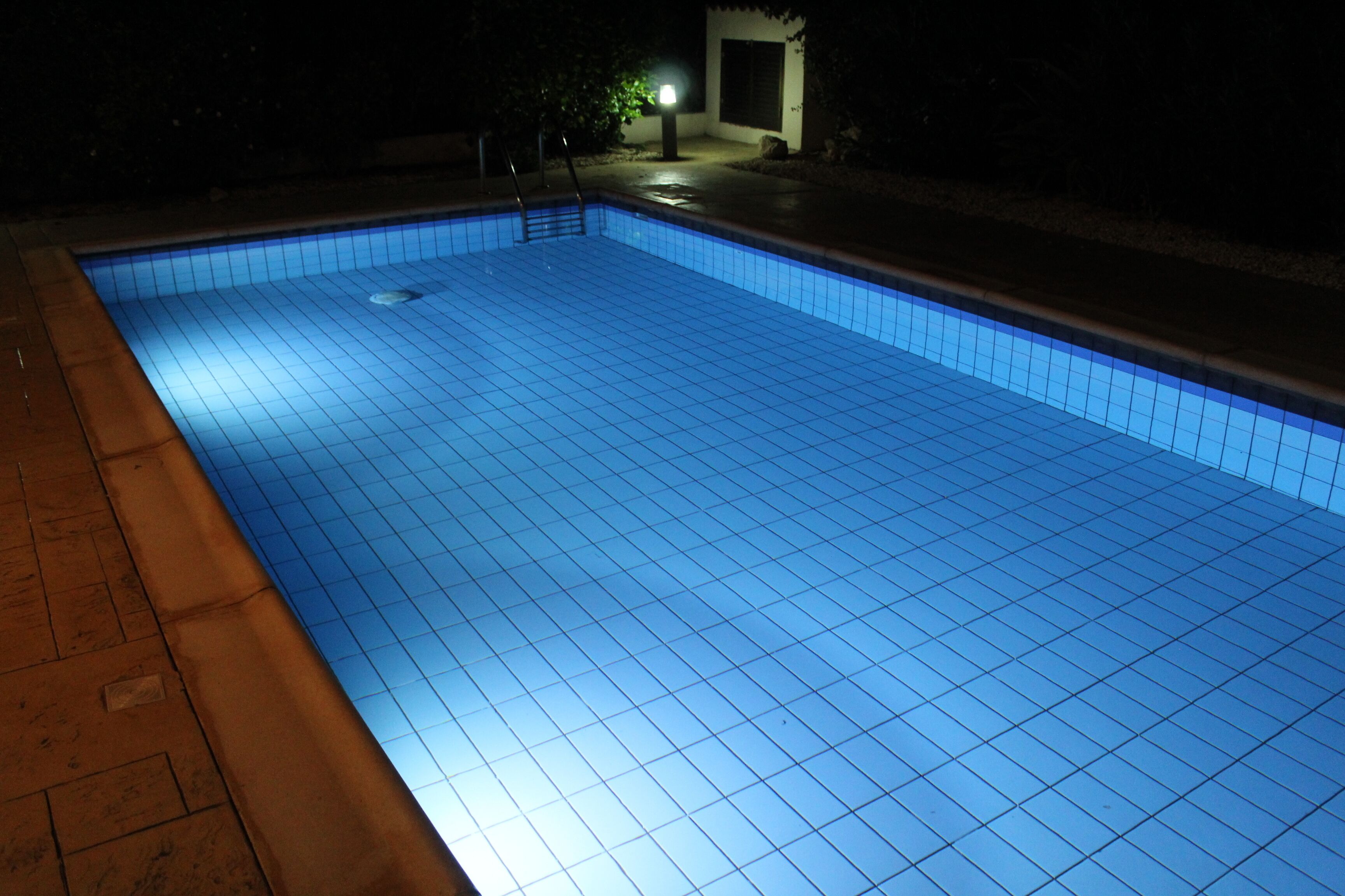 A swimming pool at night with tiled edges and a small pool ladder.
