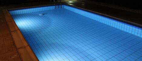 A swimming pool at night with tiled edges and a small pool ladder.