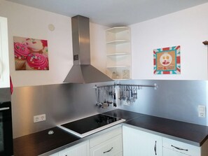 A kitchen with a stainless steel range hood, a black induction cooktop, and hanging utensils. - Haus Susanne - self-catered Guest House Apartment. (Radstadt)