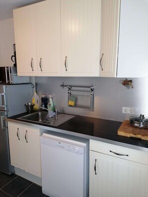 A kitchen with white cabinets, a stainless steel sink, a dish rack, and a dishwasher.