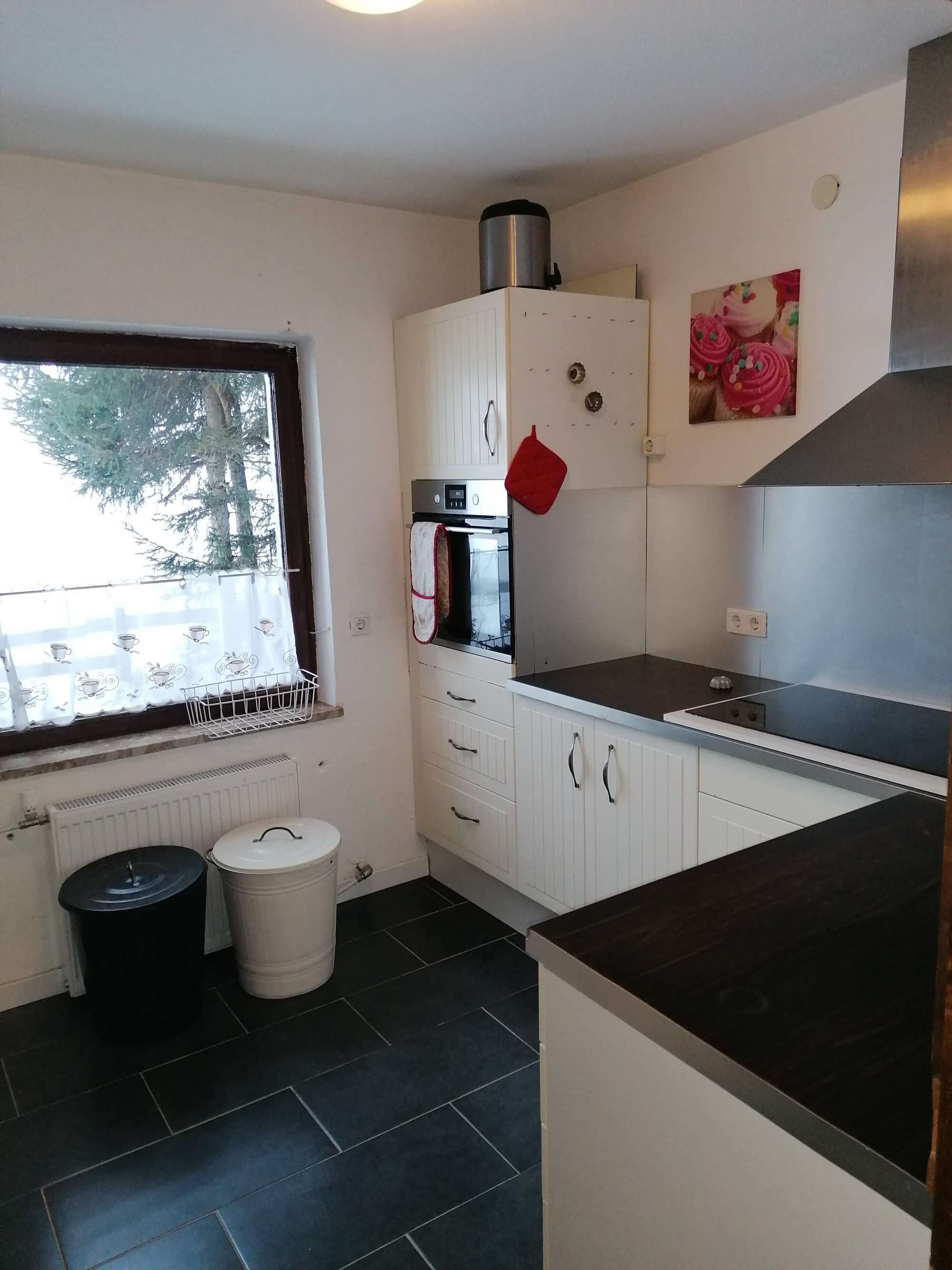 Cocina compacta con horno empotrado, hornilla y ventana con vista a árboles.