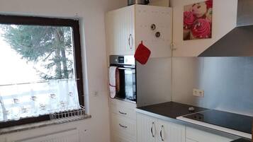 Cocina compacta con horno empotrado, hornilla y ventana con vista a árboles.