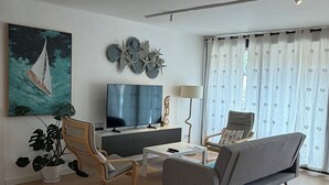 Una sala de estar moderna con un sofá, dos sillones, una mesa de centro, un televisor, una planta y un cuadro.