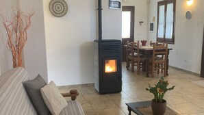 A cozy living room with a fireplace, a sofa with cushions, a dining area with chairs, and a potted plant on a table. - Casa Nerelie S big garden for playing, wi-fi free!!I - IT091063C2000P2044 (Orosei)