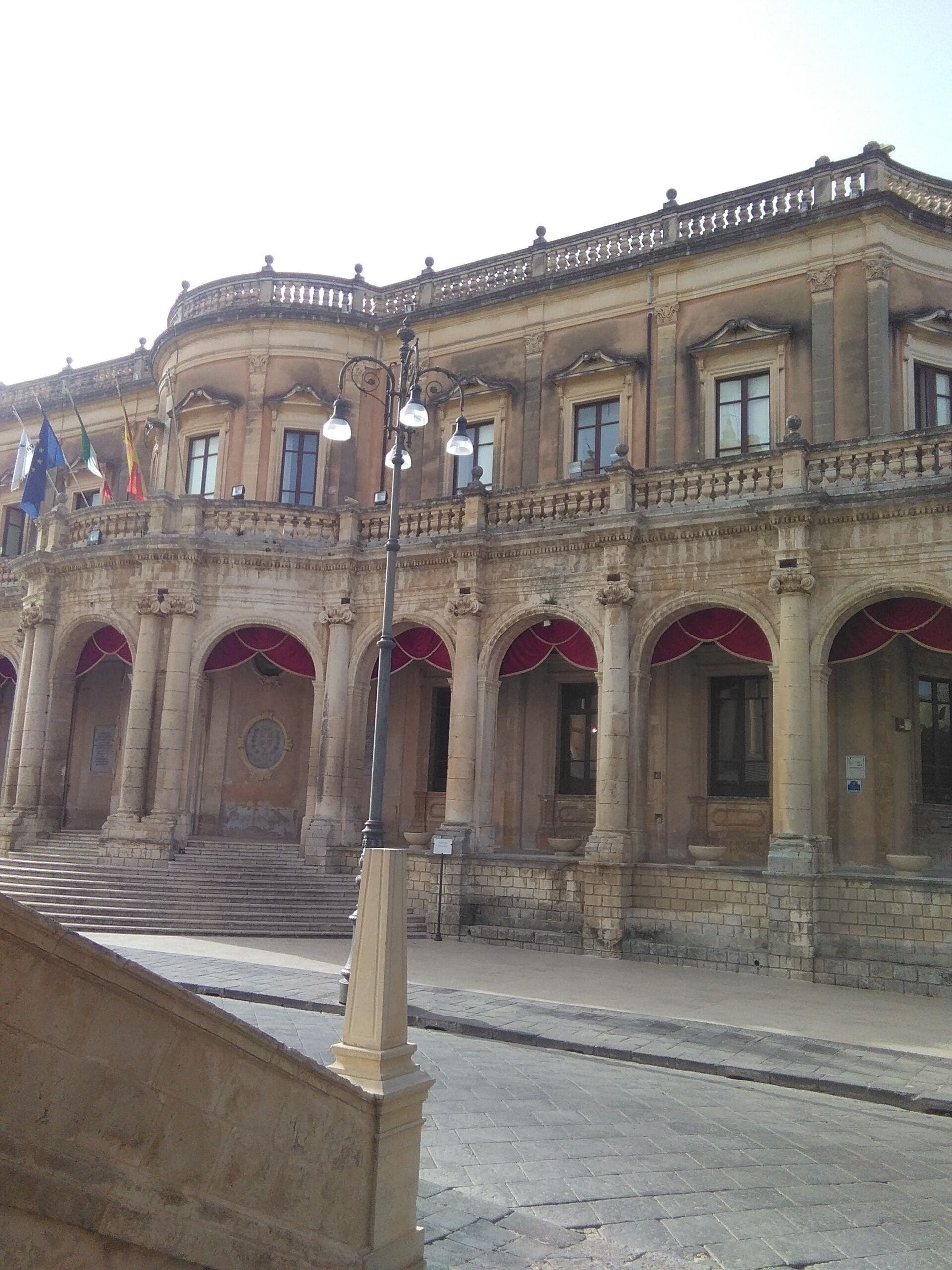 A historic building with a classical architectural style, featuring a central entrance with red awnings and multiple windows.