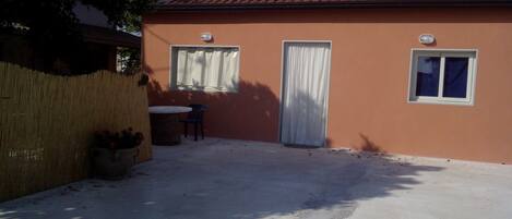 A single-story building with a tiled roof, a covered patio area with a table and chairs, and a fenced yard.