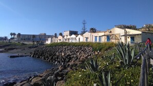 A coastal area with a rocky shoreline, buildings with blue doors, and a clear sky.