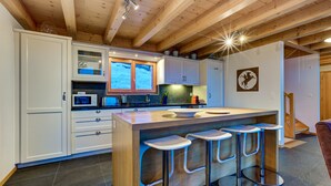 Een moderne keuken met witte kasten, een houten kookeiland met barstoelen en een groot raam.