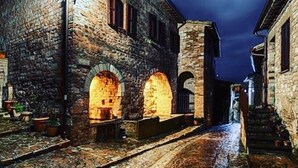 A narrow stone pathway leading to a building with arched doorways and a person standing at the end. - Villa Elisa Historical residence Welness (Spello)