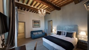 A bedroom with a large bed, a blue sofa, a chandelier, and a television. - Villa Elisa Historical residence Welness (Spello)
