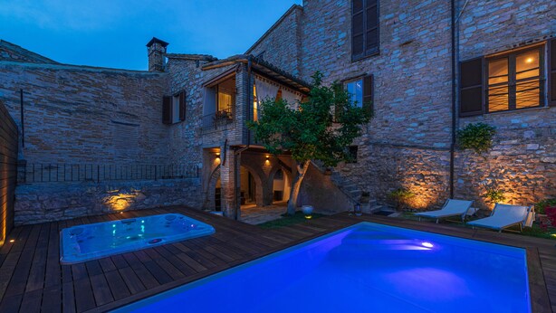 A stone building with a swimming pool, wooden deck, and outdoor seating area. - Villa Elisa Historical residence Welness (Spello)