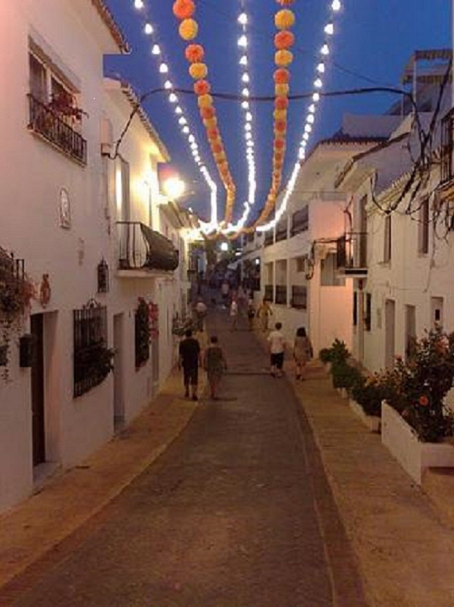 A narrow street with buildings on either side, decorated with string lights.