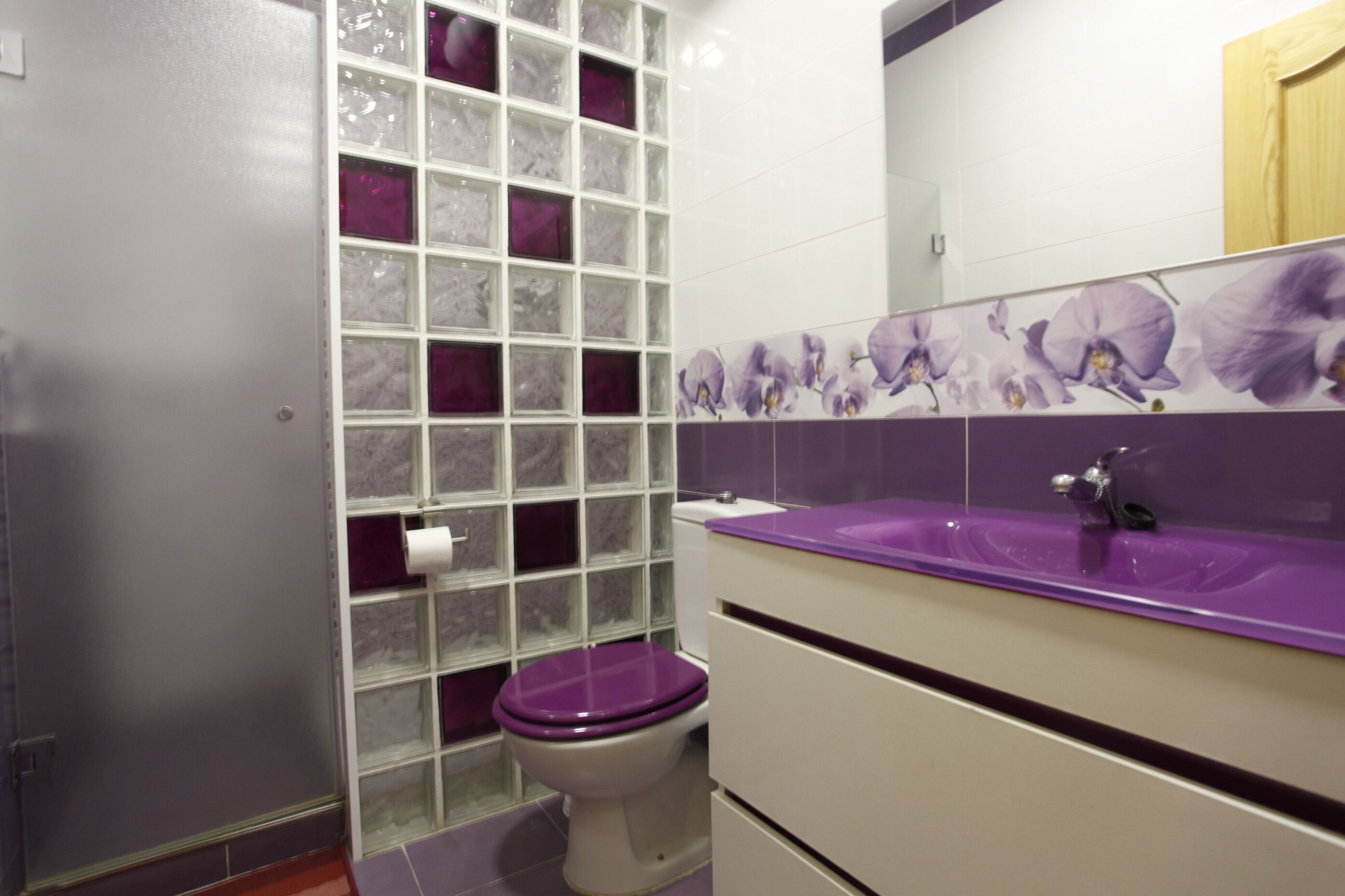 A bathroom with a toilet, a glass shower enclosure, and a sink with a purple countertop.