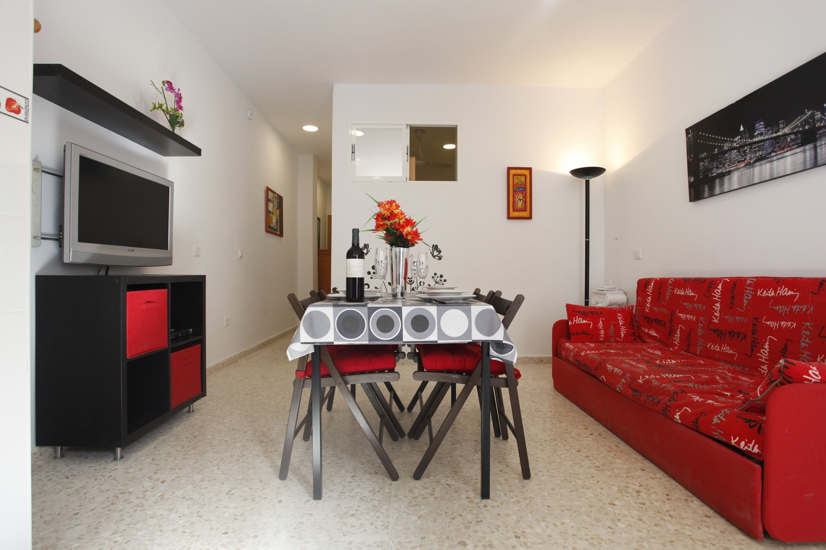 Un comedor con una mesa, sillas, un televisor y un sofá rojo.