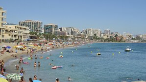 Une plage où l’on voit des gens nager et bronzer, un bateau sur l’eau et des bâtiments en arrière-plan.