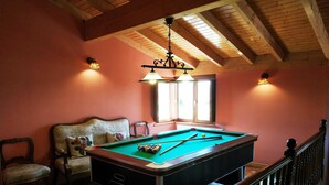 Une table de billard dans une pièce aux poutres apparentes et ornée d’un lustre.