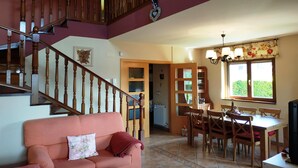 Un vaste espace de vie agrémenté d’un escalier en bois, d’une table à manger avec des chaises, d’un canapé avec un coussin et d’un lustre.