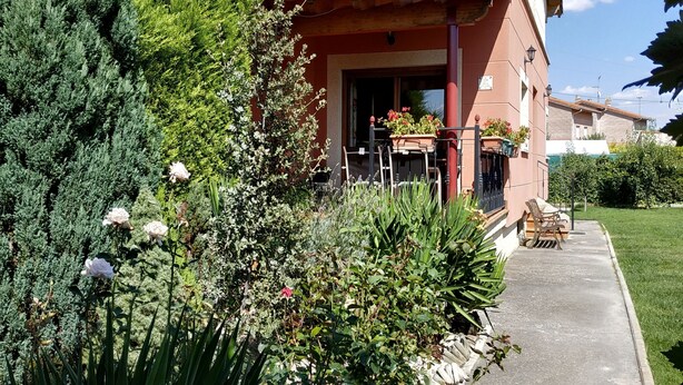 Un bâtiment à deux étages doté d’un balcon, entouré d’une végétation luxuriante et bordé d’un chemin pavé.