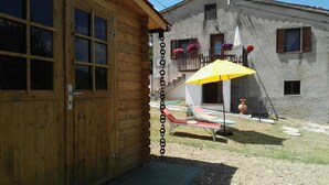 Una cabaña de madera con balcón, una sombrilla amarilla y un pequeño jardín con una silla y una mesa.