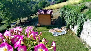 Un jardín con una pequeña estructura de madera, un parterre floral y una zona de césped con un muro de piedra.