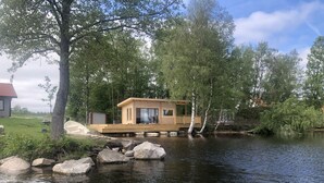 Eine Holzhütte mit einer Veranda, gelegen an einem stillen See, umgeben von Bäumen.