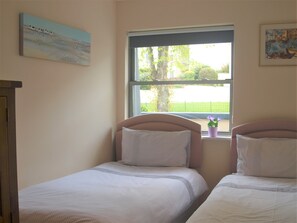 A bedroom with two single beds, a window with a view of greenery, and artwork on the walls. - Sea Front Penthouse Torquay (Torquay)