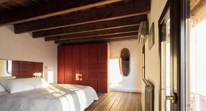 A bedroom with a wooden floor, a bed with a white bedspread, a red wardrobe, and a radiator.