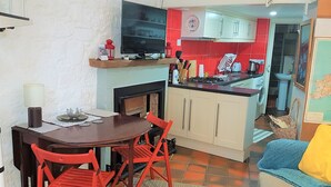 Una cocina compacta con comedor, un televisor montado sobre la encimera y una pequeña zona de estar con un sofá y una silla.