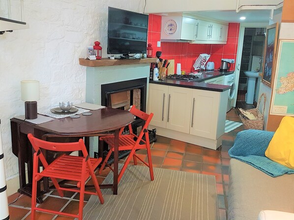 A compact kitchen with a dining area, a TV mounted above the counter, and a small seating area with a sofa and a chair. - Auld Pottery - Charming & Central gem in the heart of the city centre (Edinburgh)