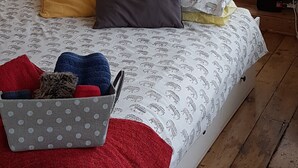 Un dormitorio con cama, almohadas, una mesita de noche, una lámpara y una ventana con vistas a una lavadora y muebles de exterior.