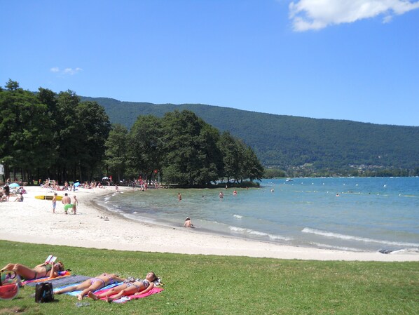 A beach with people sunbathing and swimming, surrounded by trees and hills.