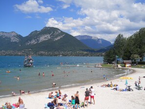 A beach with people sunbathing and swimming, a lifeguard tower, and mountains in the background.