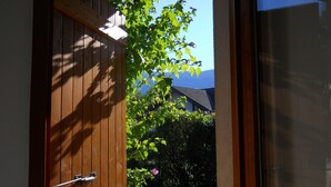 A wooden door with a metal handle, leading to a garden with a lawn and a tree with green leaves and pink flowers. - T3. 2 Bed Apart Private Garden, 200m to beach. super fast wifi. cheap bikes (Saint-Jorioz)
