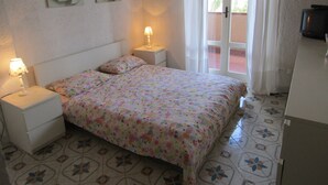 A bedroom with a bed, two nightstands, a lamp, a television, and a window with curtains. - relax in the green near the sea and from the center of Forio (Forio)