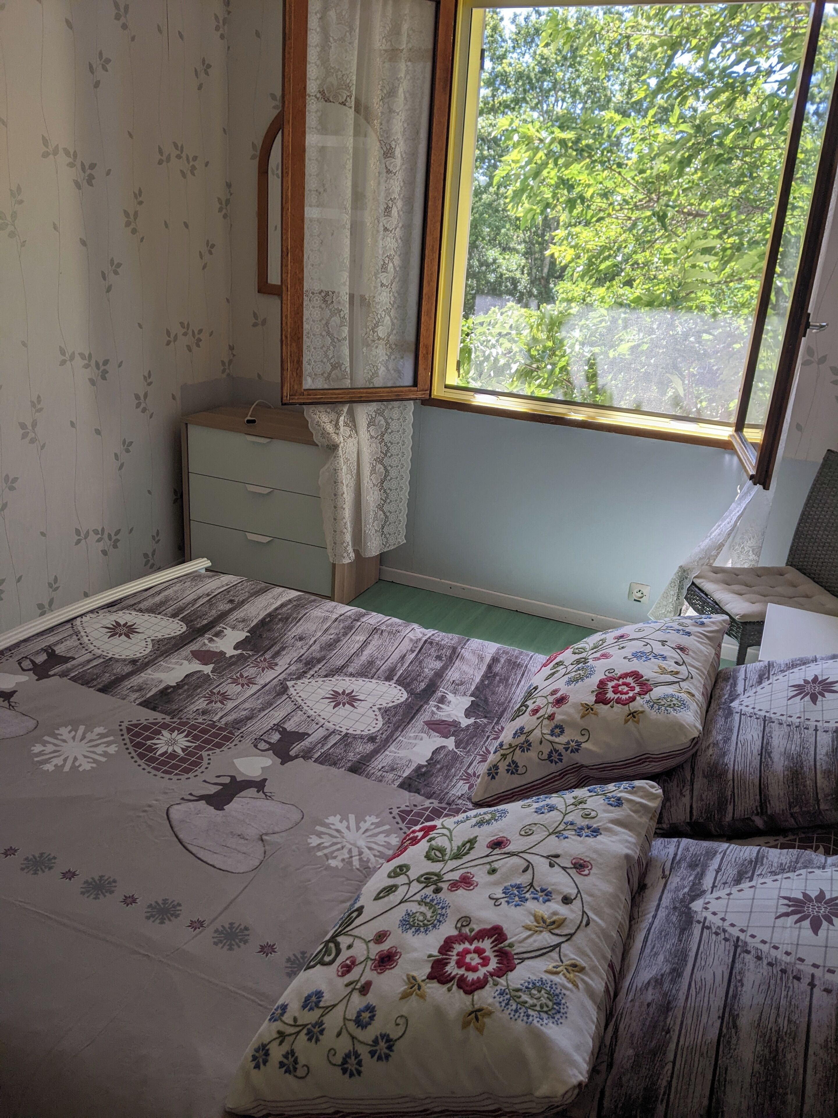 Une chambre à coucher avec un lit en bois, une literie à motifs floraux, une table de chevet et une fenêtre donnant sur un paysage verdoyant.