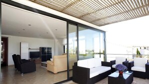 A modern living room with a glass wall, a flat-screen TV, and a sofa set. - Luxury apartment with beautiful views, private pool and beach access (Portocolom)