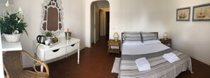 Quarto com cama, mesas de cabeceira, cômoda, espelho e uma planta em vaso.