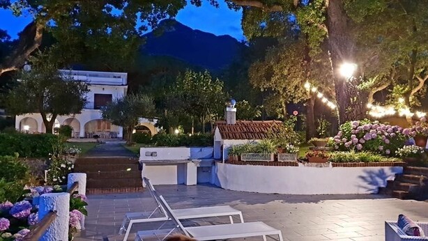 Un patio con un camino adoquinado, sillas de descanso y un pequeño edificio con techo de tejas.