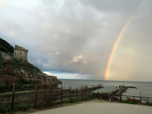 A coastal scene with a castle-like structure, a wooden pier, and a rainbow over the sea. - Villa Francesca Romana<br>Relax by the lake a few meters from the sea (Sabaudia)