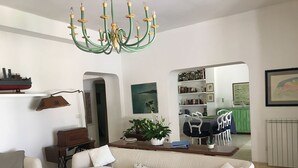 Una sala de estar con una araña verde, un sofá blanco, un comedor con una mesa verde y una cocina visible a través de un arco.